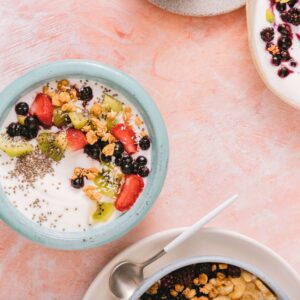 Top view of colorful yogurt bowls topped with fresh berries and granola on a rustic background.